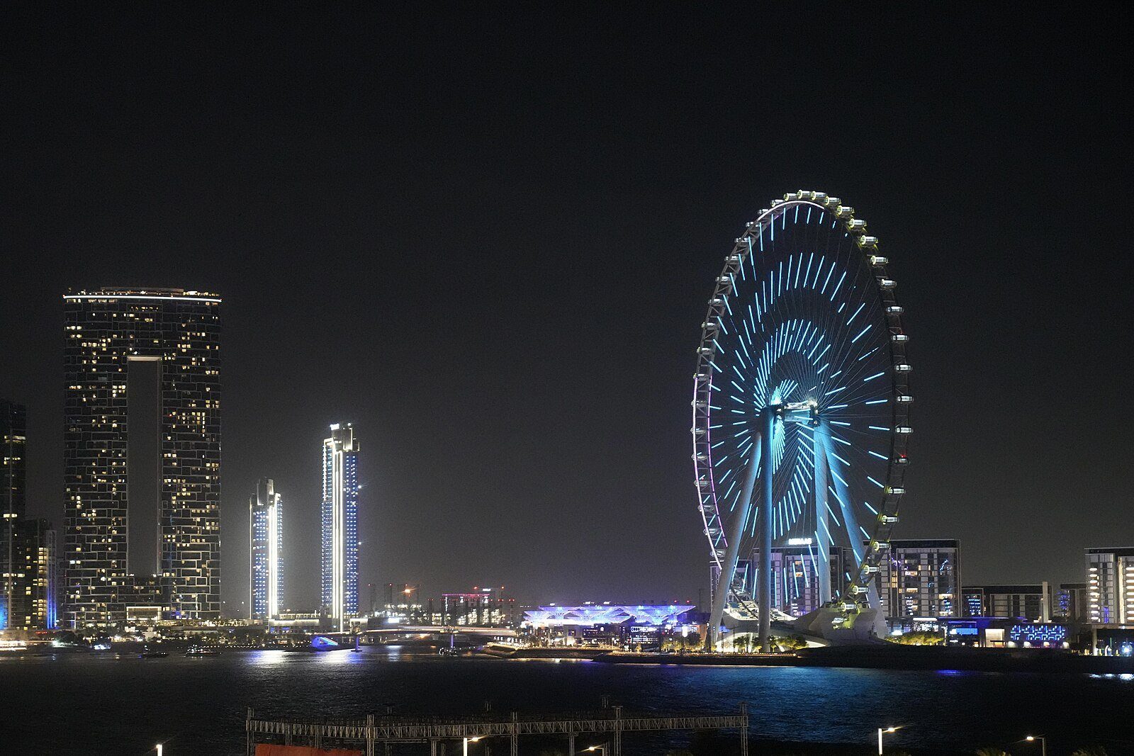 La Ain Dubai, iluminada en azul en Bluewaters Island, junto a las torres resplandecientes del frente marítimo de JBR de noche.