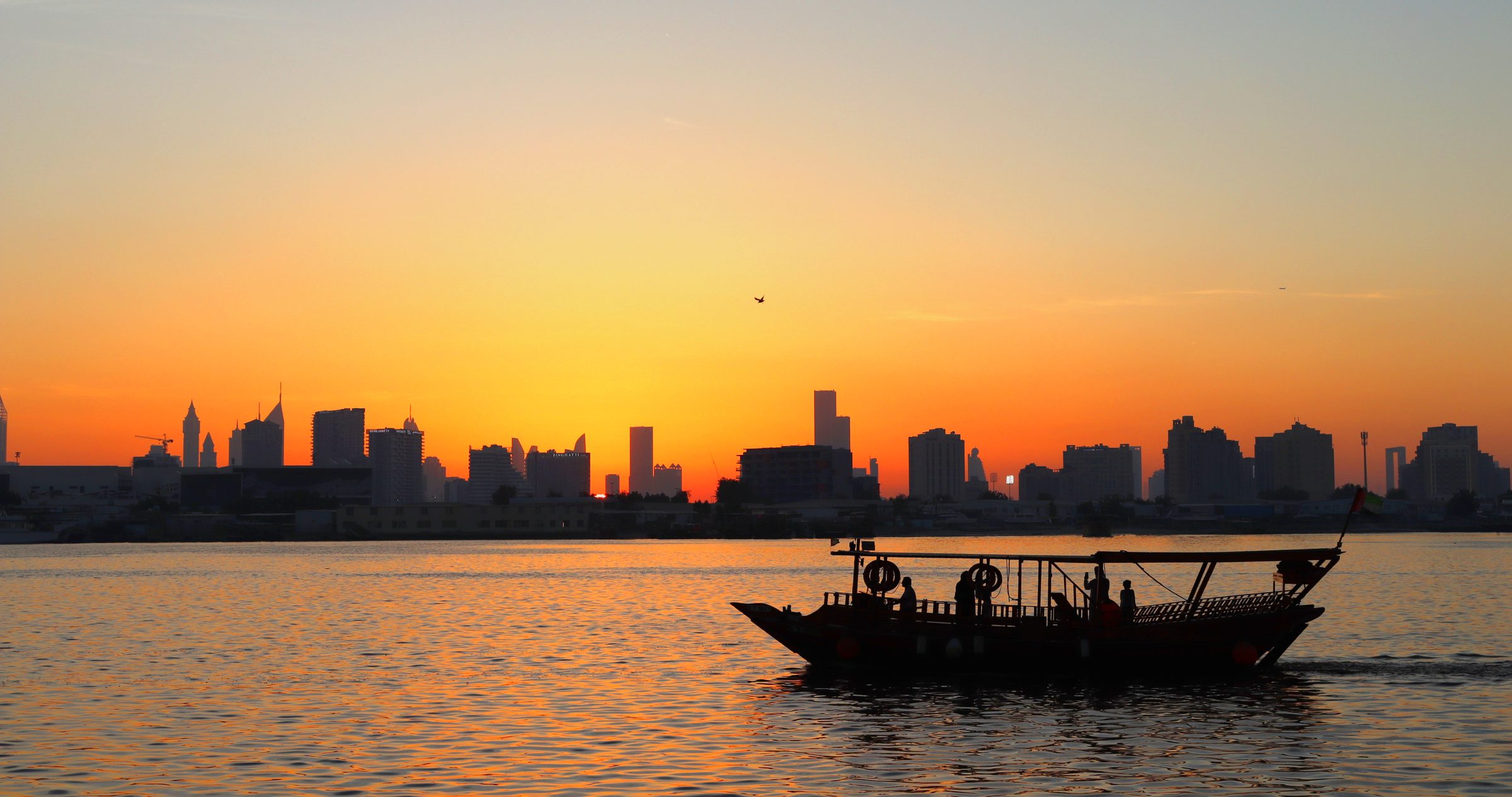 Un dhow tradicional cruza el Dubai Creek bajo el perfil urbano al atardecer