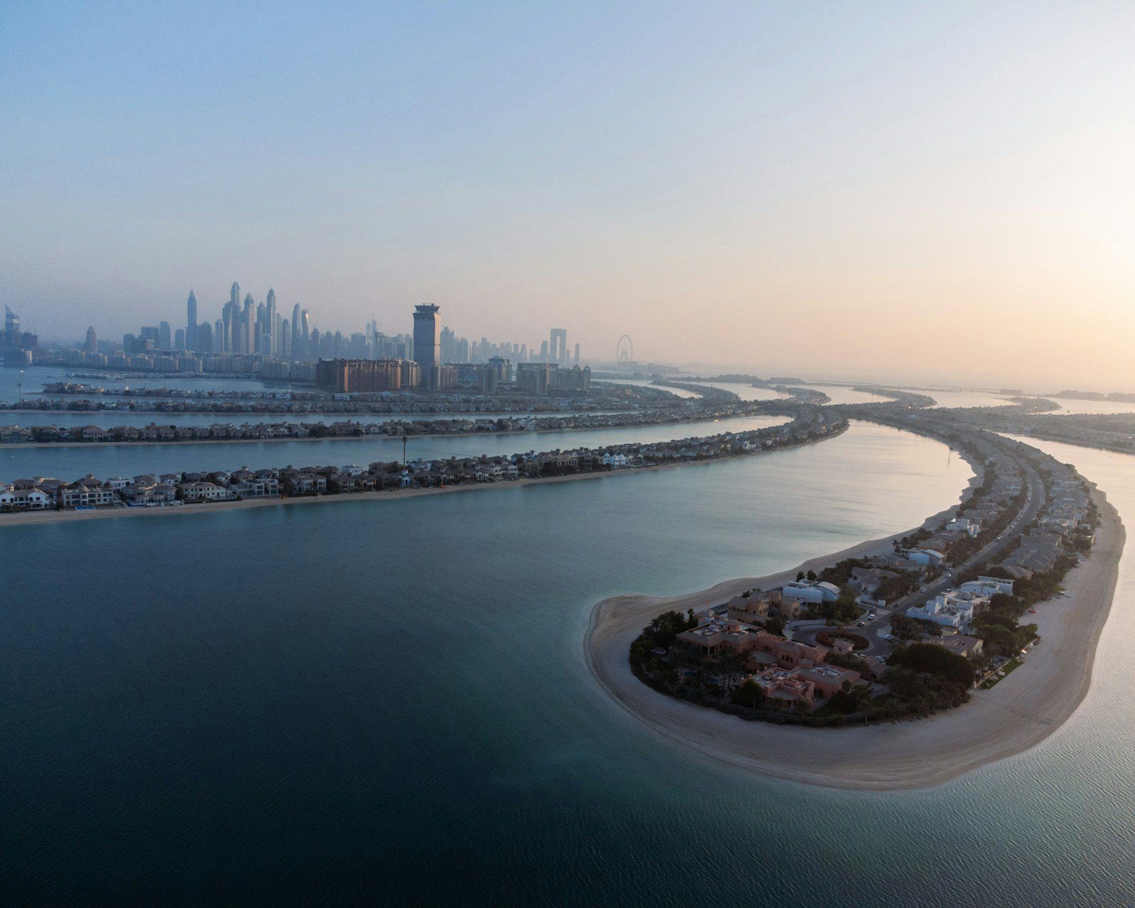 Villas frente a la playa jalonan las frondas curvas de Palm Jumeirah al amanecer, con las torres de Dubai Marina en el horizonte