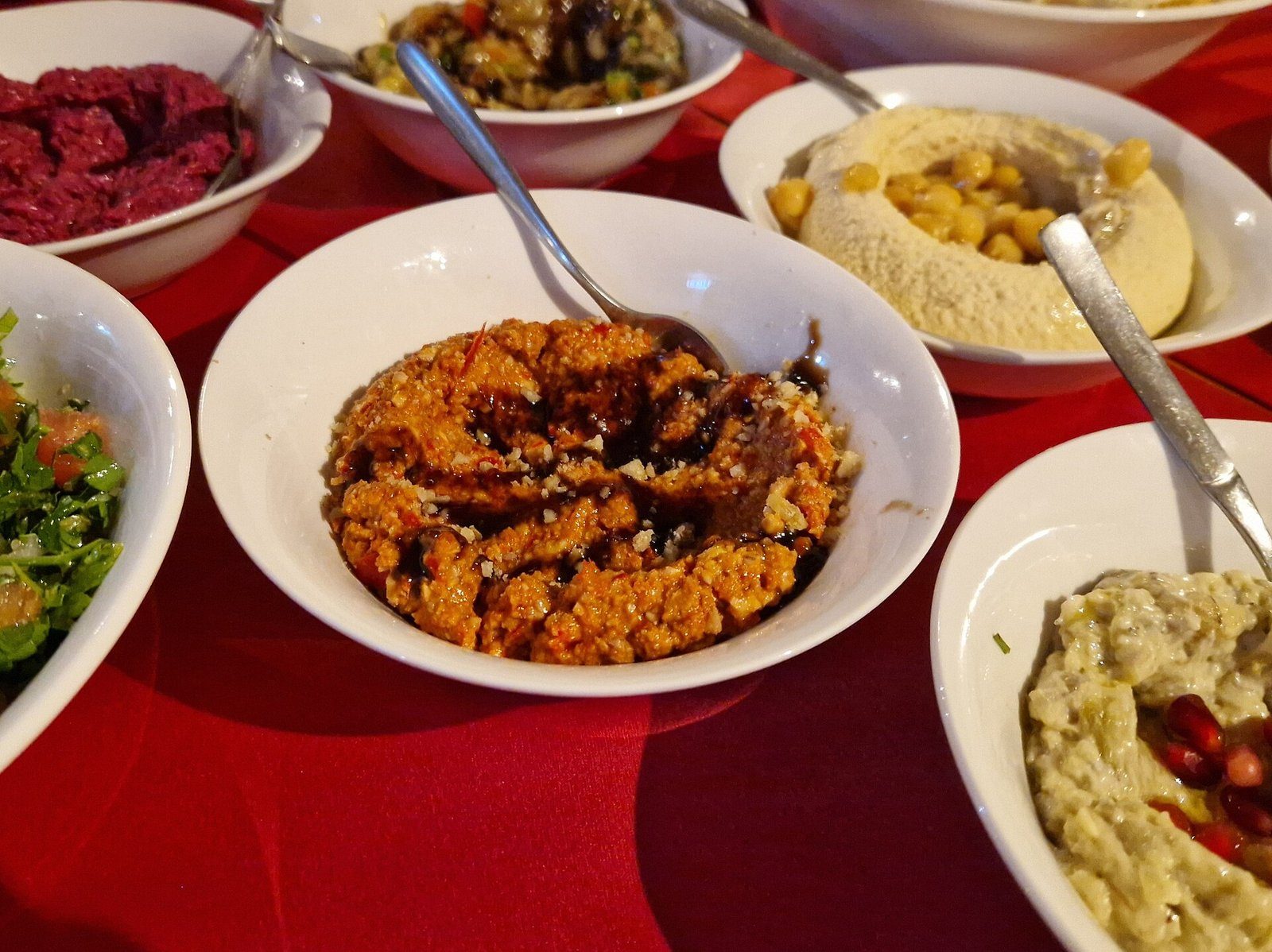 Una mesa de mezze libaneses: hummus, muhammara, baba ganoush y fattoush en cuencos blancos.
