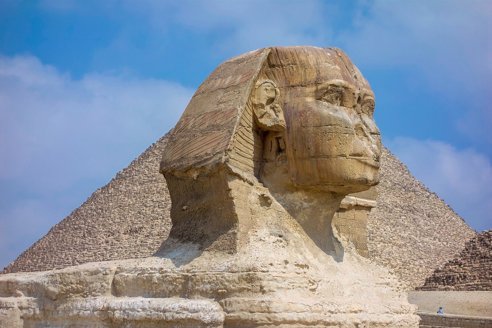 La cabeza de la Gran Esfinge de perfil frente a la Gran Pirámide de Guiza y un suave cielo azul