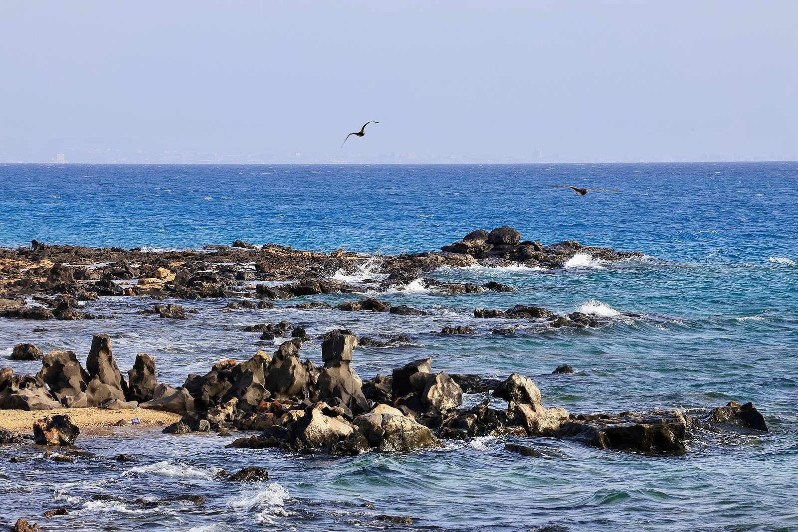 Aguas azul transparente del Mar Rojo rompiendo sobre oscuras rocas volcánicas en la playa de Harrat, Umluj, en la costa noroeste de Arabia Saudí.