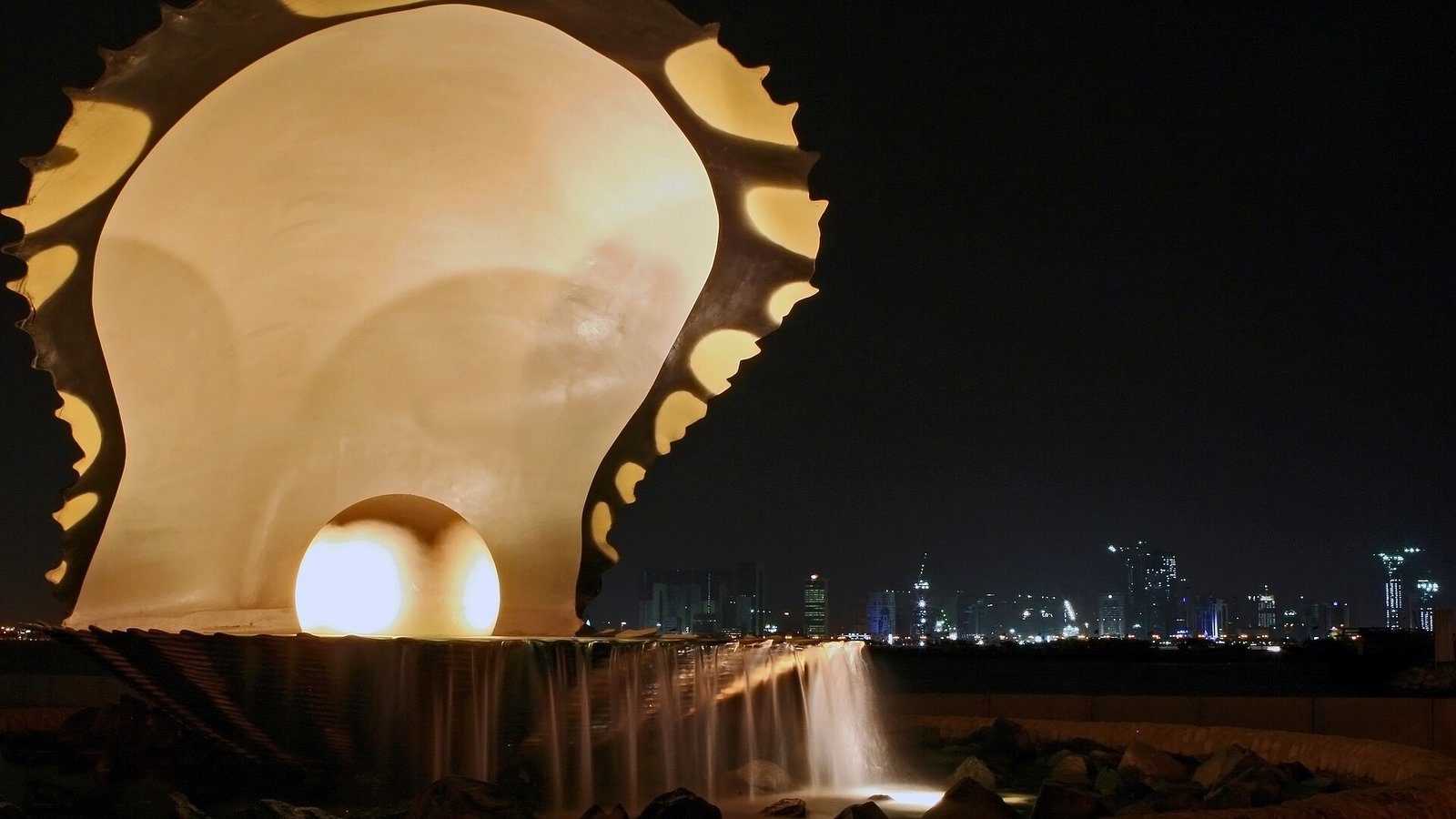 El Monumento de la Perla iluminado, una concha de ostra que acuna una perla resplandeciente, en la Corniche de Doha de noche.