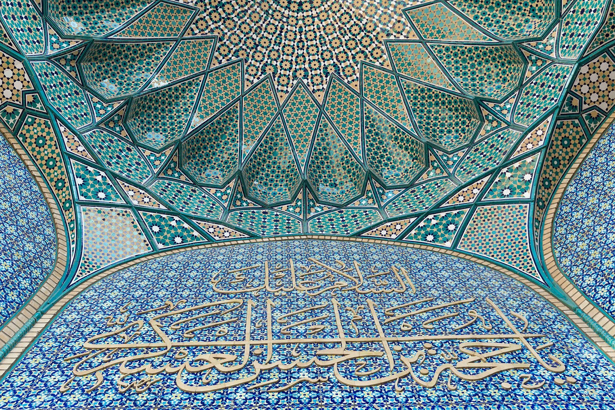 Caligrafía y azulejería geométrica turquesa bajo el pórtico de una mezquita