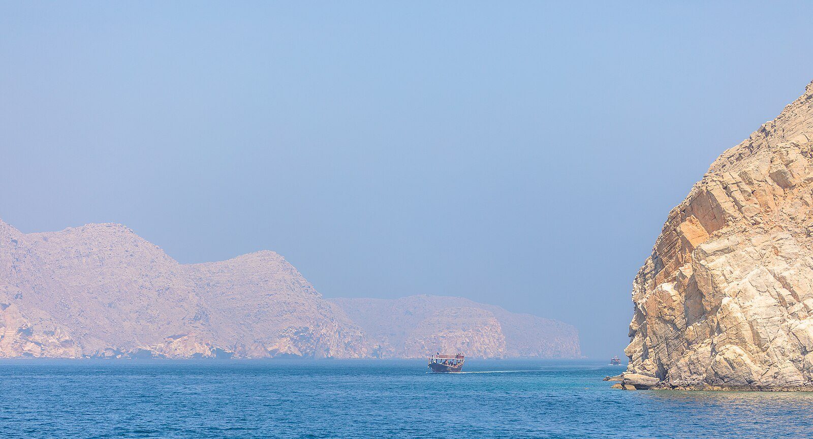 Un dhow surcando las aguas azules de los fiordos de Musandam bajo escarpados acantilados de caliza, Omán.