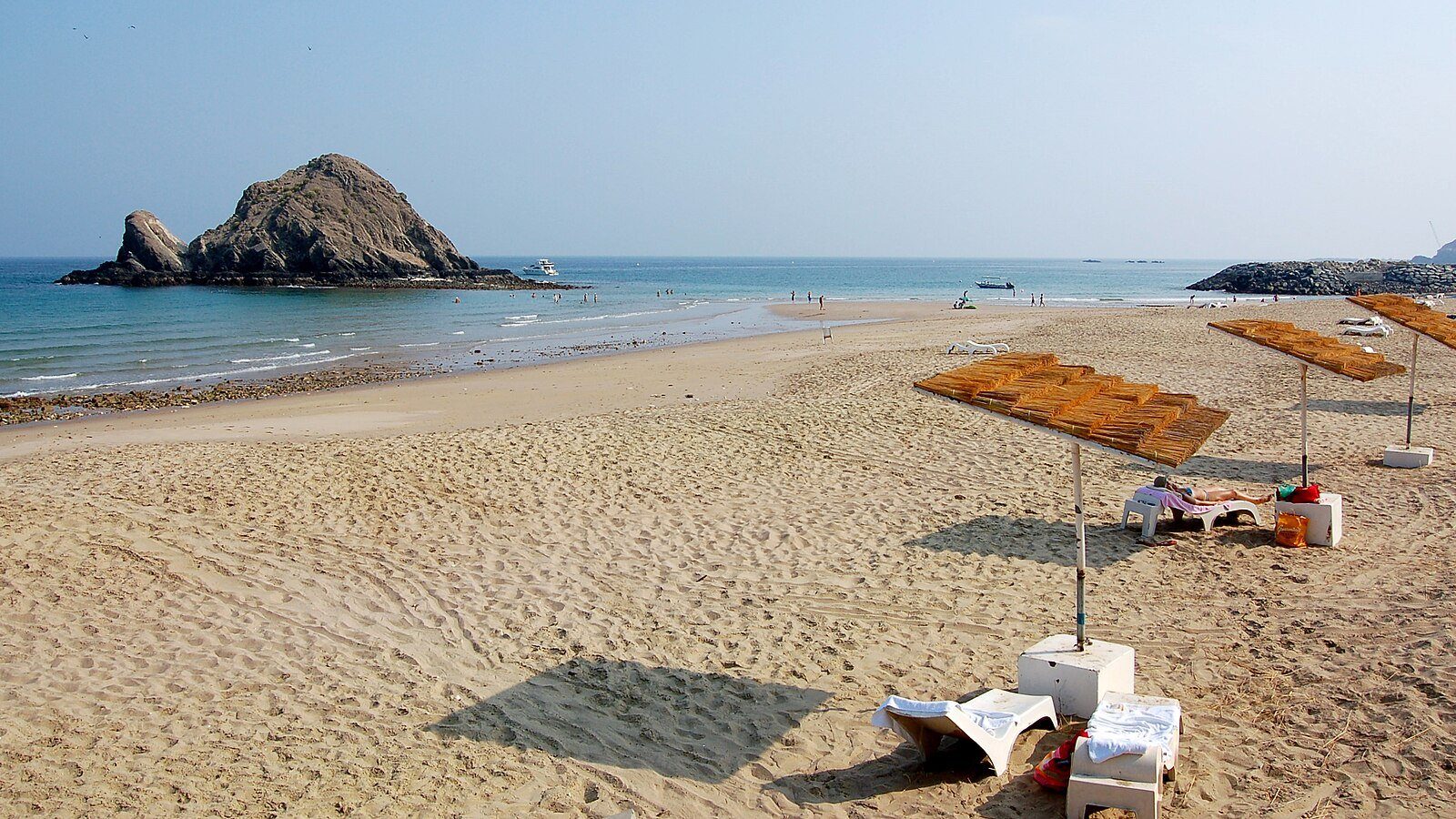 Tumbonas a la sombra sobre la arena dorada de la playa de Al Aqah, frente a Snoopy Island en el golfo de Omán