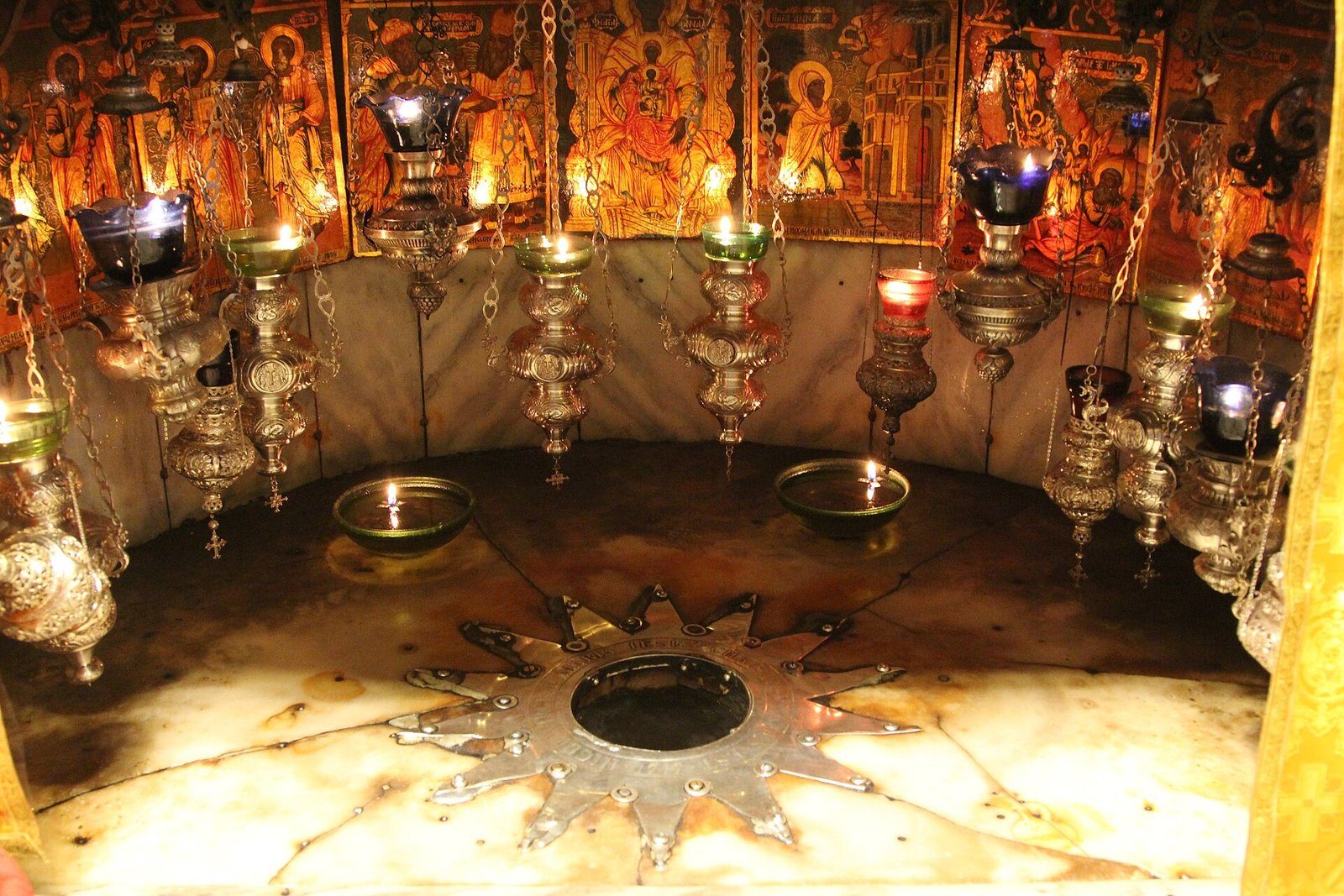 La estrella de plata que marca el lugar tradicional del nacimiento de Jesús en la Gruta de la Natividad, Belén, bajo lámparas de aceite colgantes.