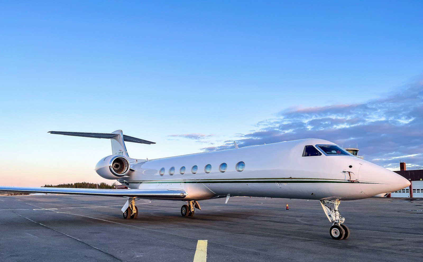 Un jet de negocios Gulfstream blanco espera en la plataforma bajo un suave cielo de atardecer.