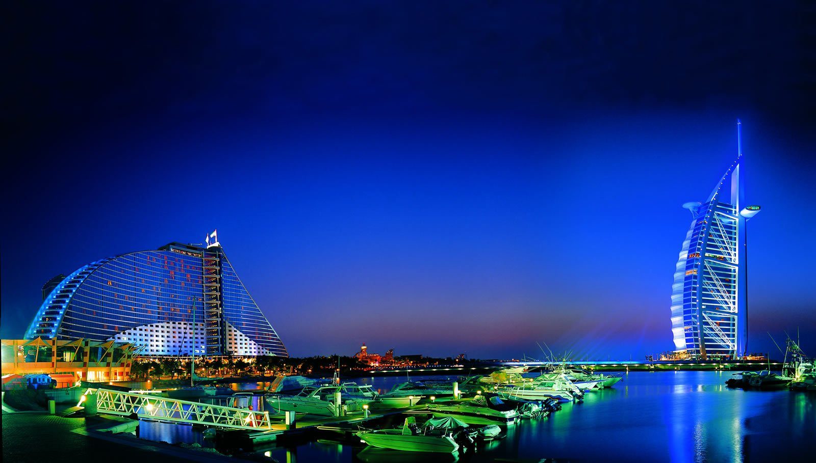 El Burj Al Arab y el Jumeirah Beach Hotel en forma de ola iluminados en la hora azul sobre la marina de Dubái.