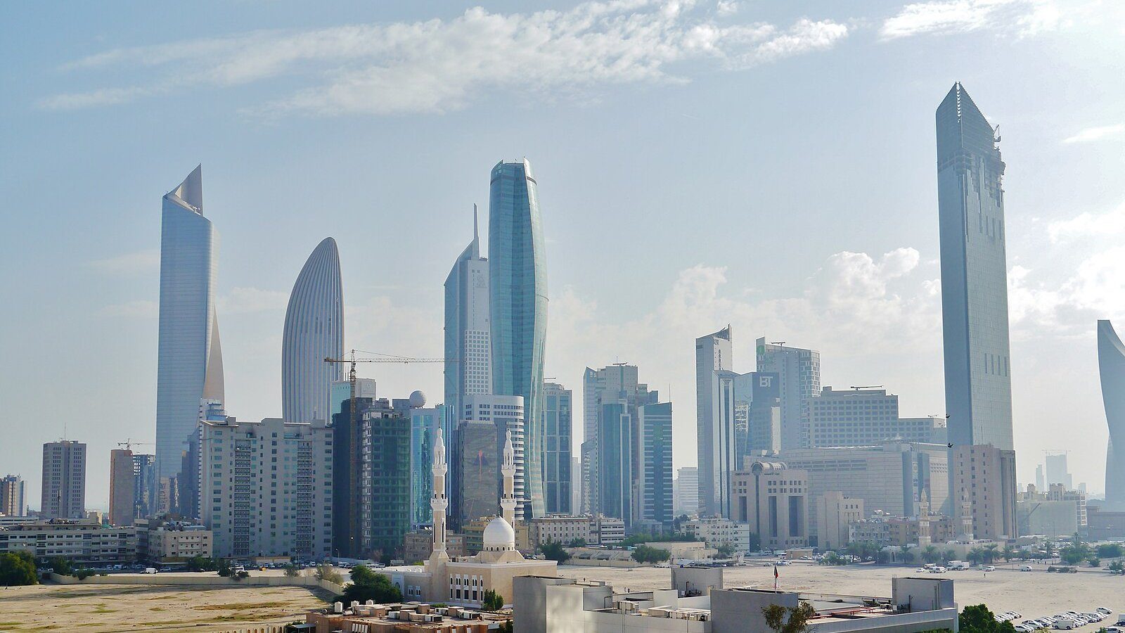Las torres de vidrio del distrito financiero central de la Ciudad de Kuwait alzándose bajo un cielo suave surcado de nubes