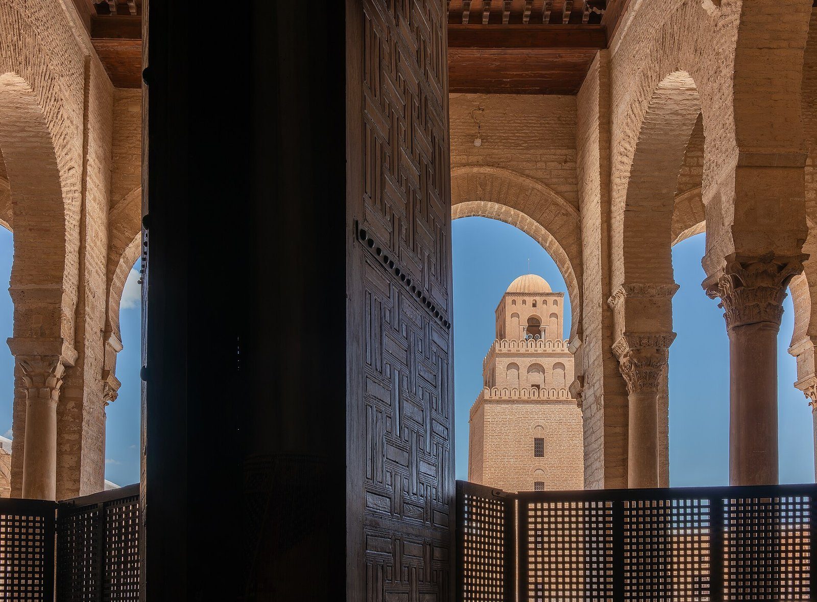 El minarete de la Gran Mezquita de Kairuán enmarcado por los arcos de herradura tallados de la galería de la sala de oración.