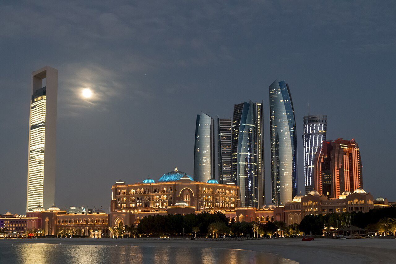 Emirates Palace y las Etihad Towers iluminados bajo la luna naciente en el frente marítimo de Abu Dabi.