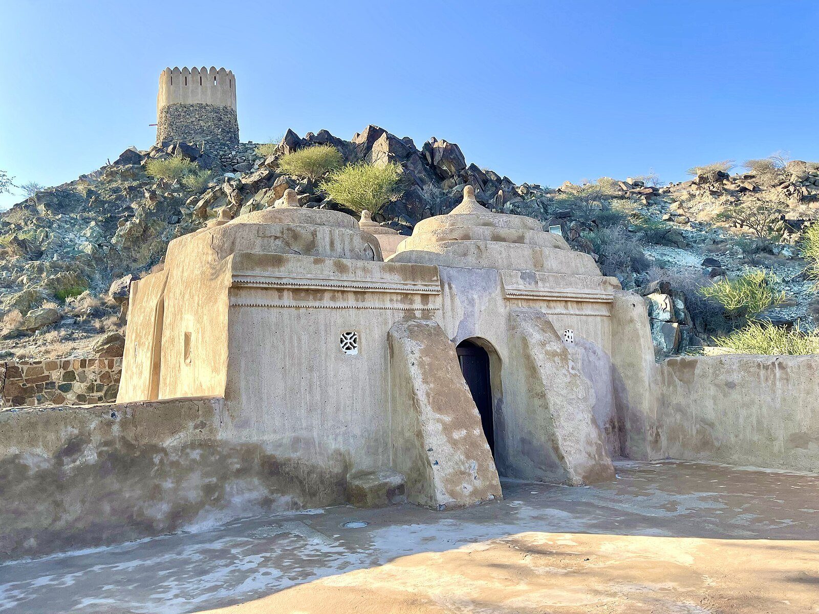 Los muros de barro y las cúpulas de la Mezquita Al Bidya, la mezquita más antigua conocida de los EAU, bajo su torre de vigilancia en lo alto de la colina