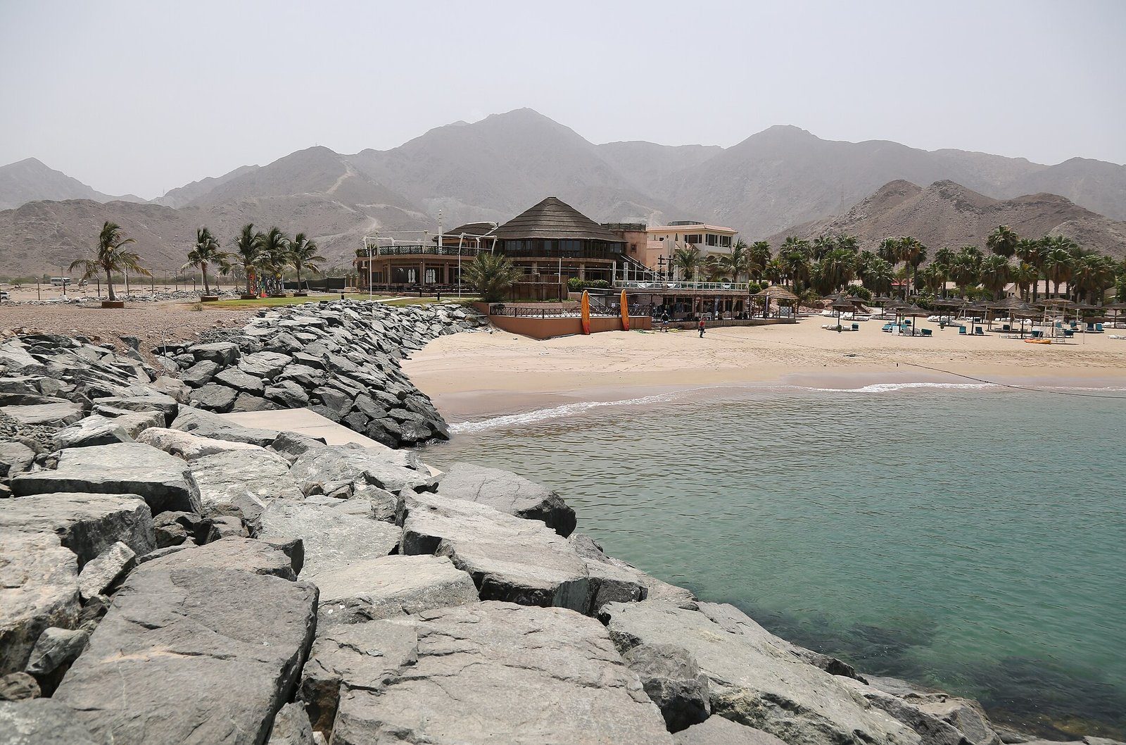 Una cala de arena resguardada y un resort bordeado de palmeras al pie de los escarpados montes Hajar, en la costa de Fujairah sobre el golfo de Omán.