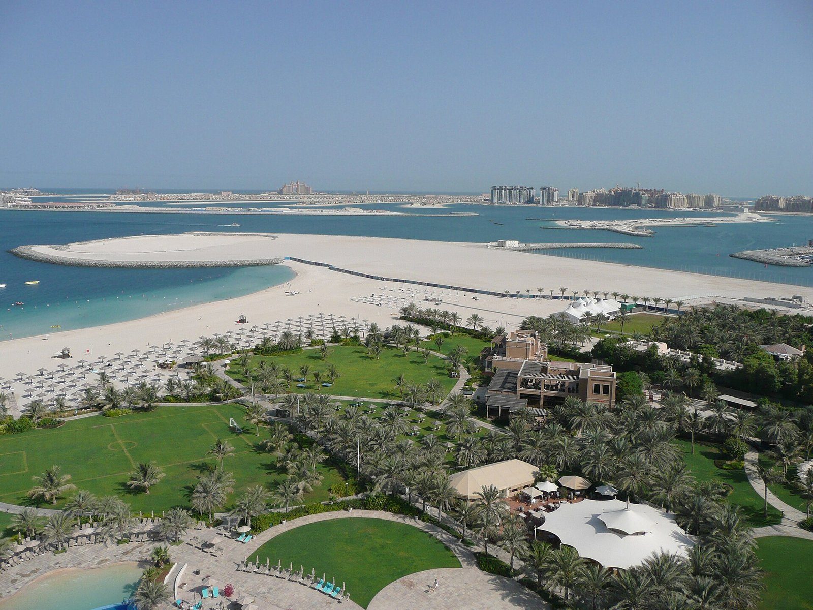 Jardines de resort y una amplia playa blanca en Dubái, con Palm Jumeirah y Atlantis en el horizonte