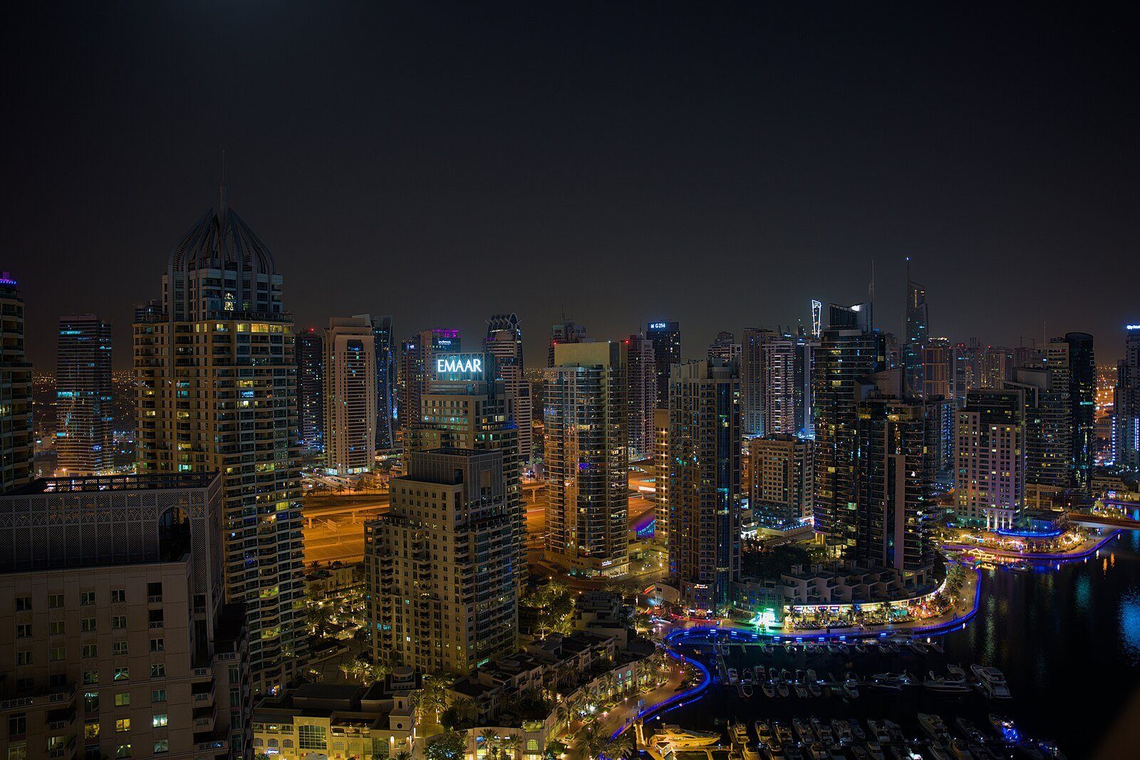 Las torres de Dubai Marina brillan de noche sobre la curva iluminada del paseo marítimo de la marina.