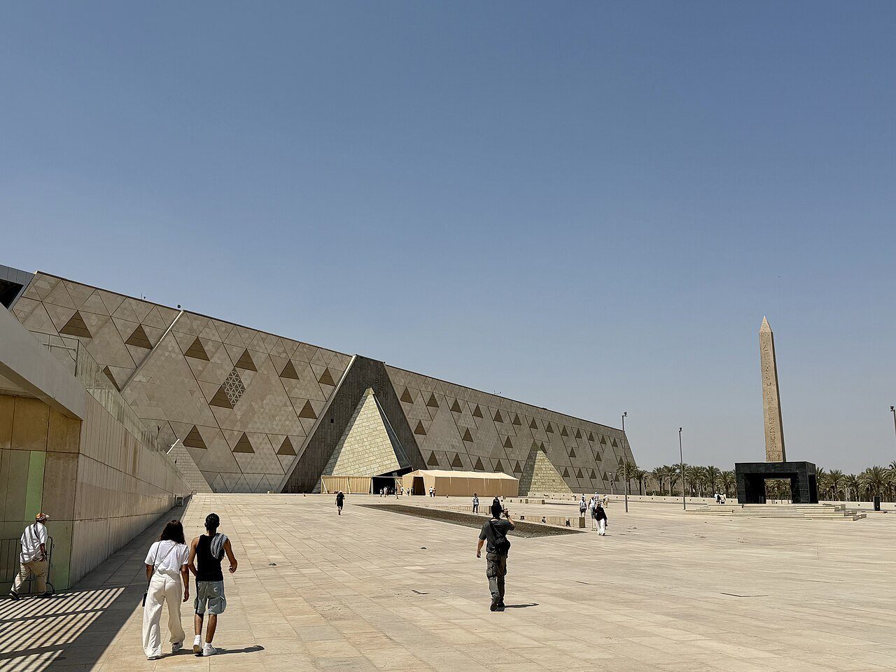 La fachada de piedra con motivos triangulares del Gran Museo Egipcio y su obelisco bajo un cielo despejado de Guiza.