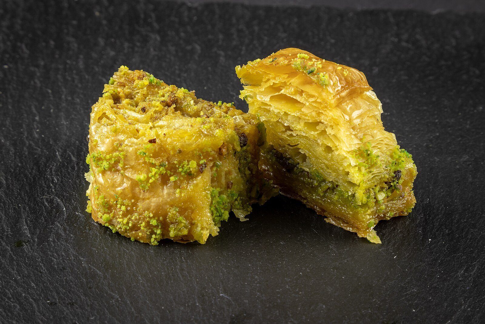 Baklava de pistacho en capas, reluciente de almíbar, sobre una pizarra oscura.