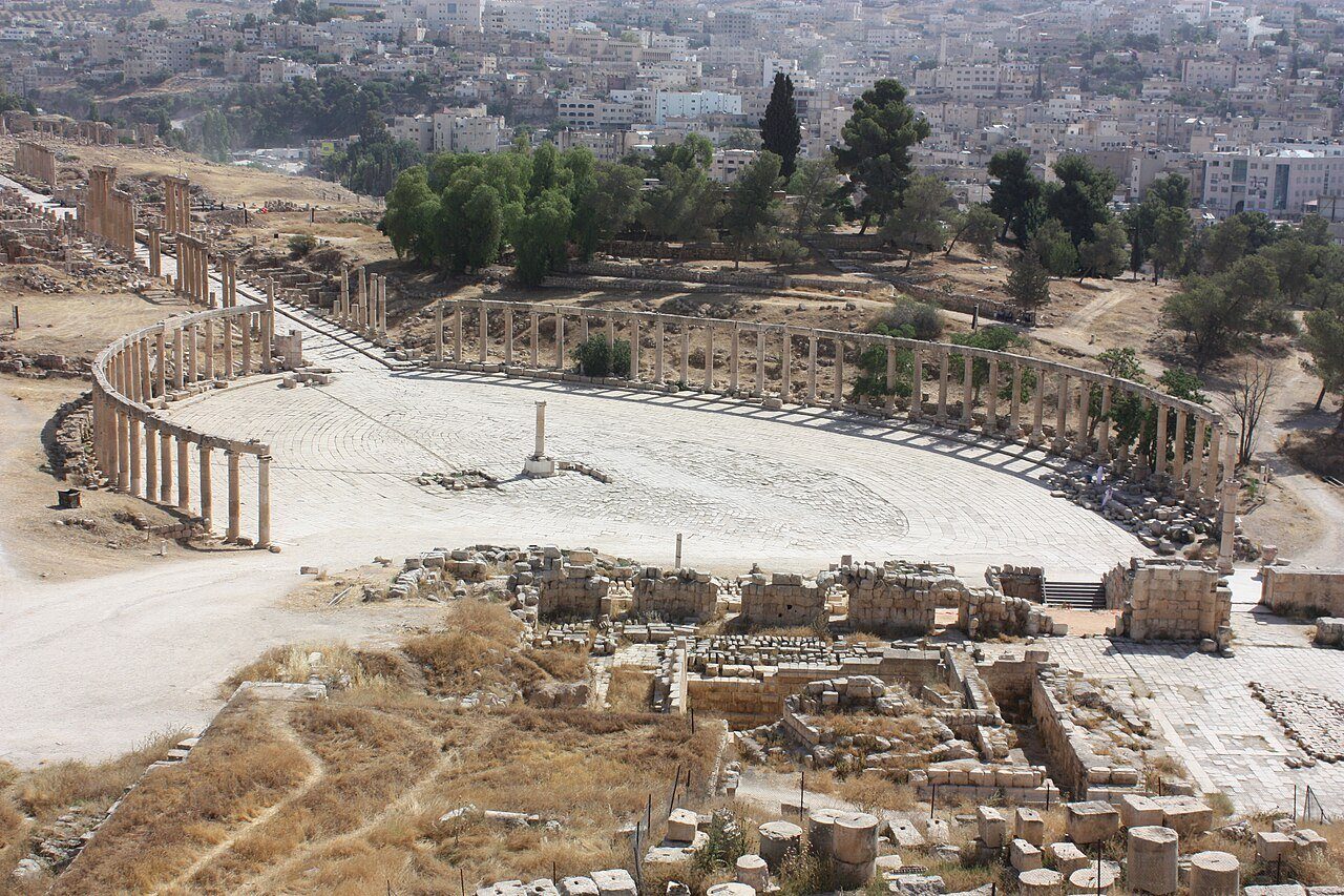 La plaza oval con columnata de la Jerash romana vista desde lo alto, con la ciudad moderna al fondo.