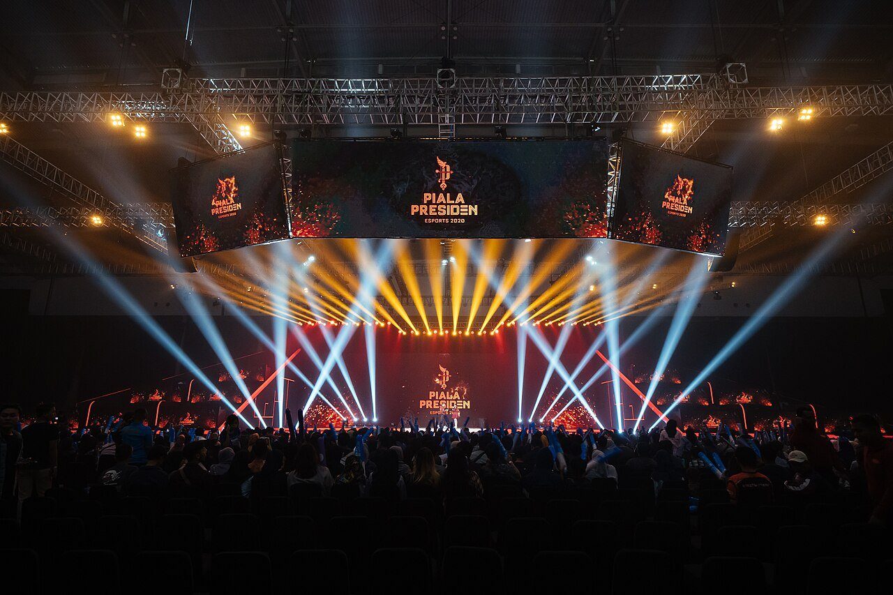 Haces de luz escénica recorren una abarrotada arena de esports durante la final de un torneo nacional.