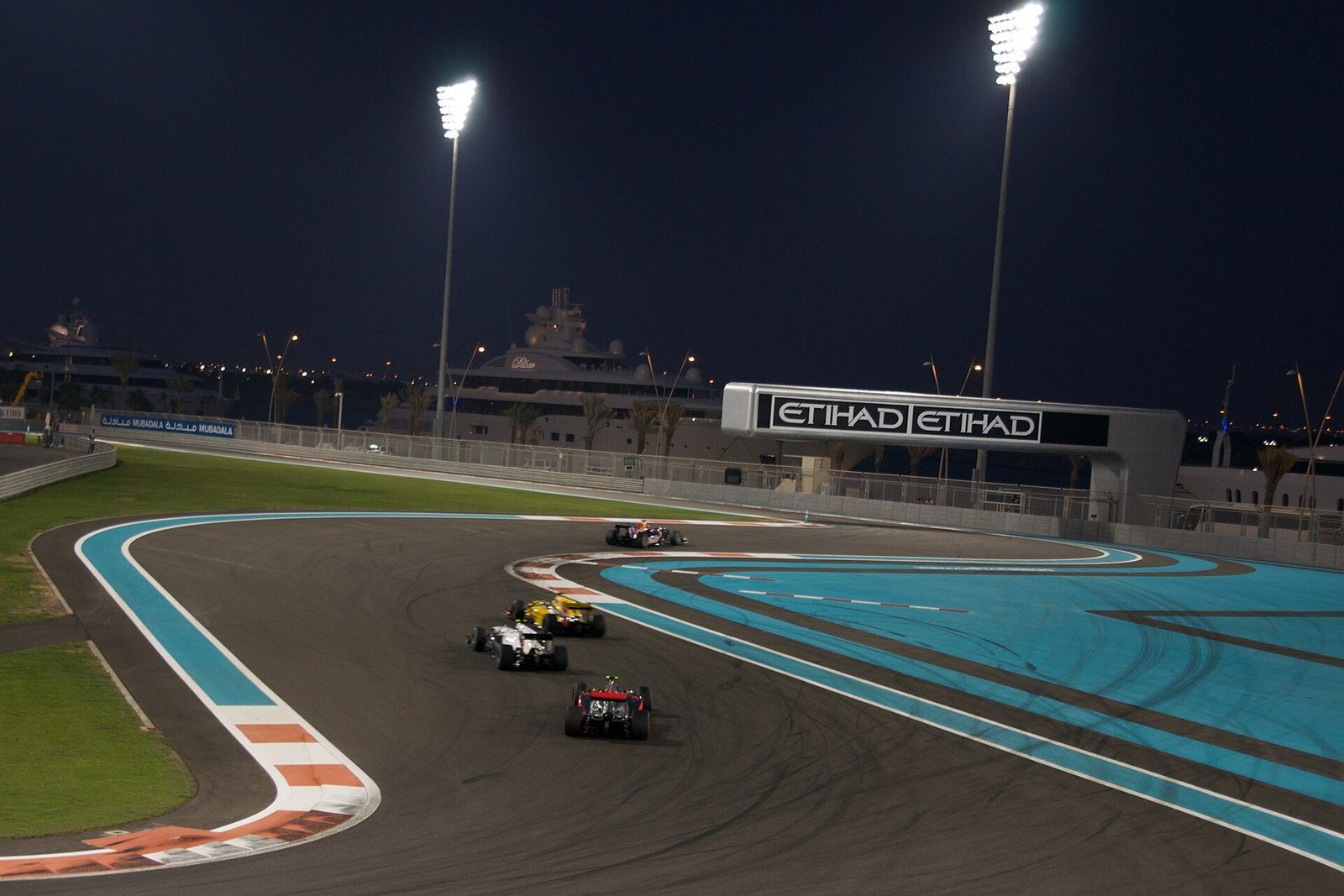 Monoplazas de Fórmula 1 compitiendo bajo los focos del circuito de Yas Marina de noche, Abu Dabi.